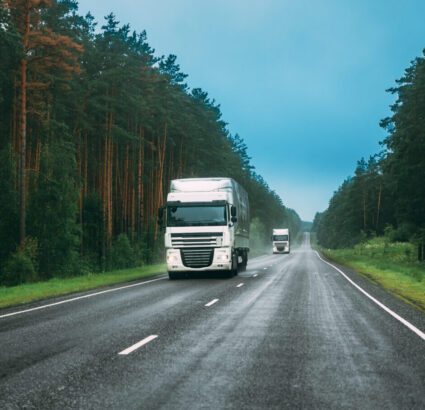 White Truck Or Tractor Unit, Prime Mover, Traction Unit In Motion On Road, Freeway. Asphalt Motorway Highway Against Background Of Forest Landscape. Business Transportation And Trucking Industry